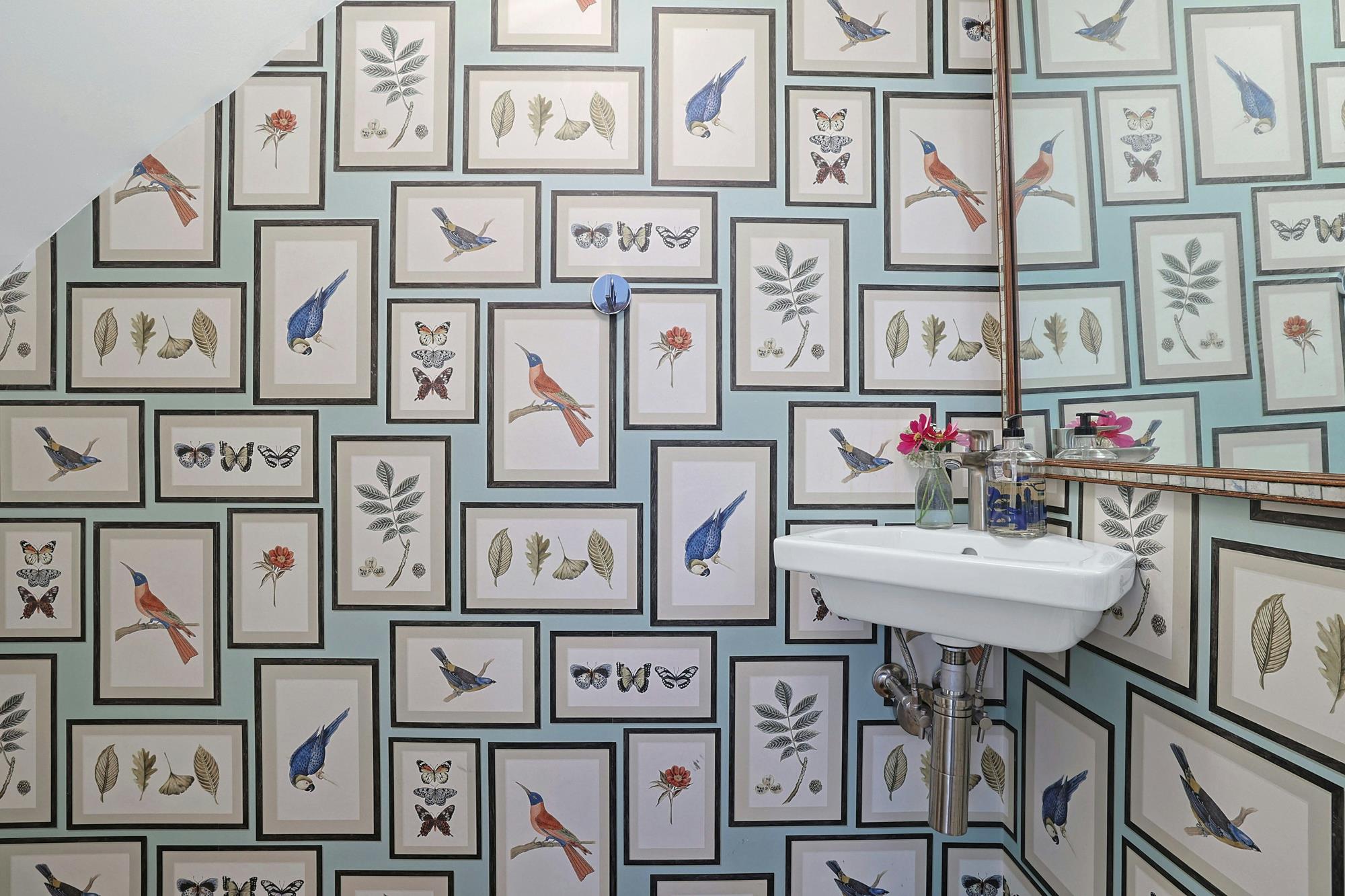 A powder room wrapped in hand-painted bird-and-botanical wallpaper.