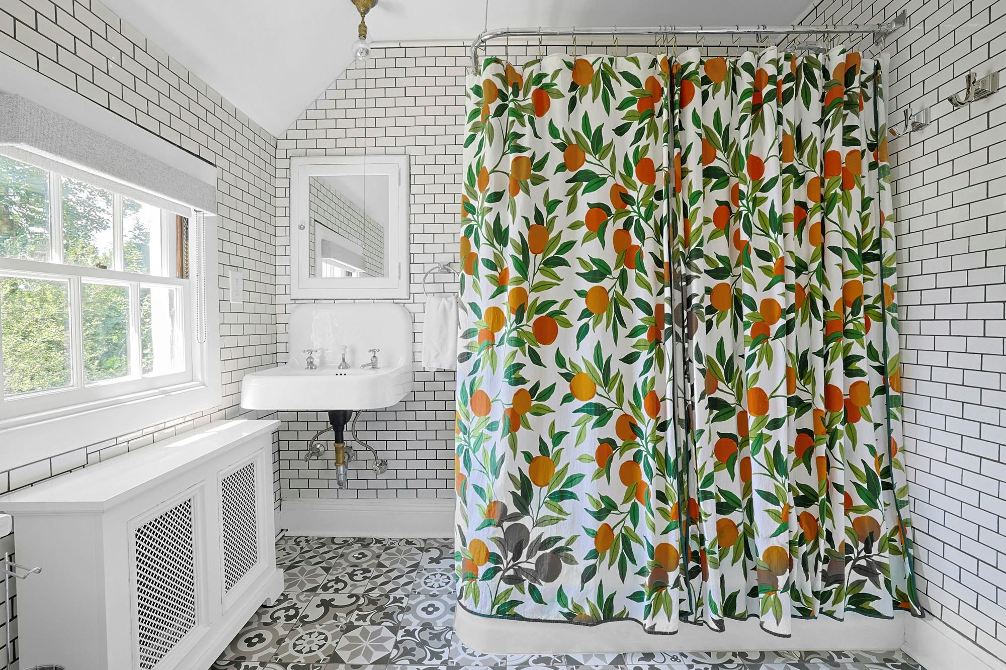 A vintage subway-tile bathroom with patterned encaustic floor and a citrus-print curtain.