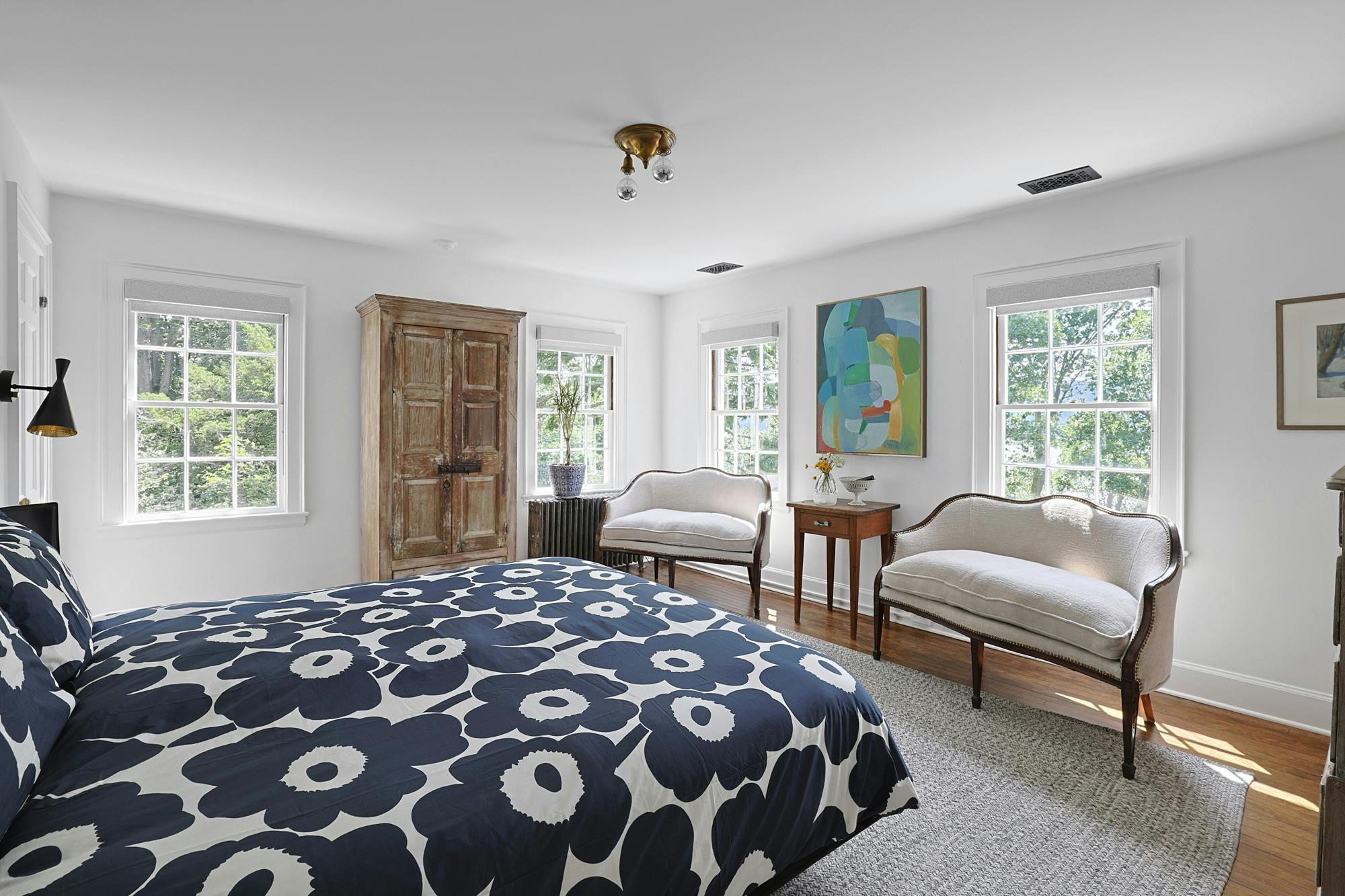 A peaceful guest bedroom with a single bed, mirrored chest, and garden-facing windows.